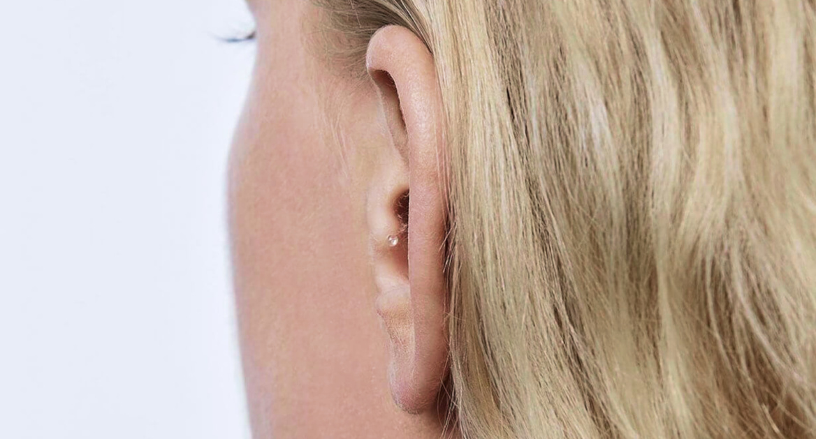 Nahaufnahme des Ohres einer Person mit blondem Haar, die ein kleines, unauffälliges Hörgerät trägt.