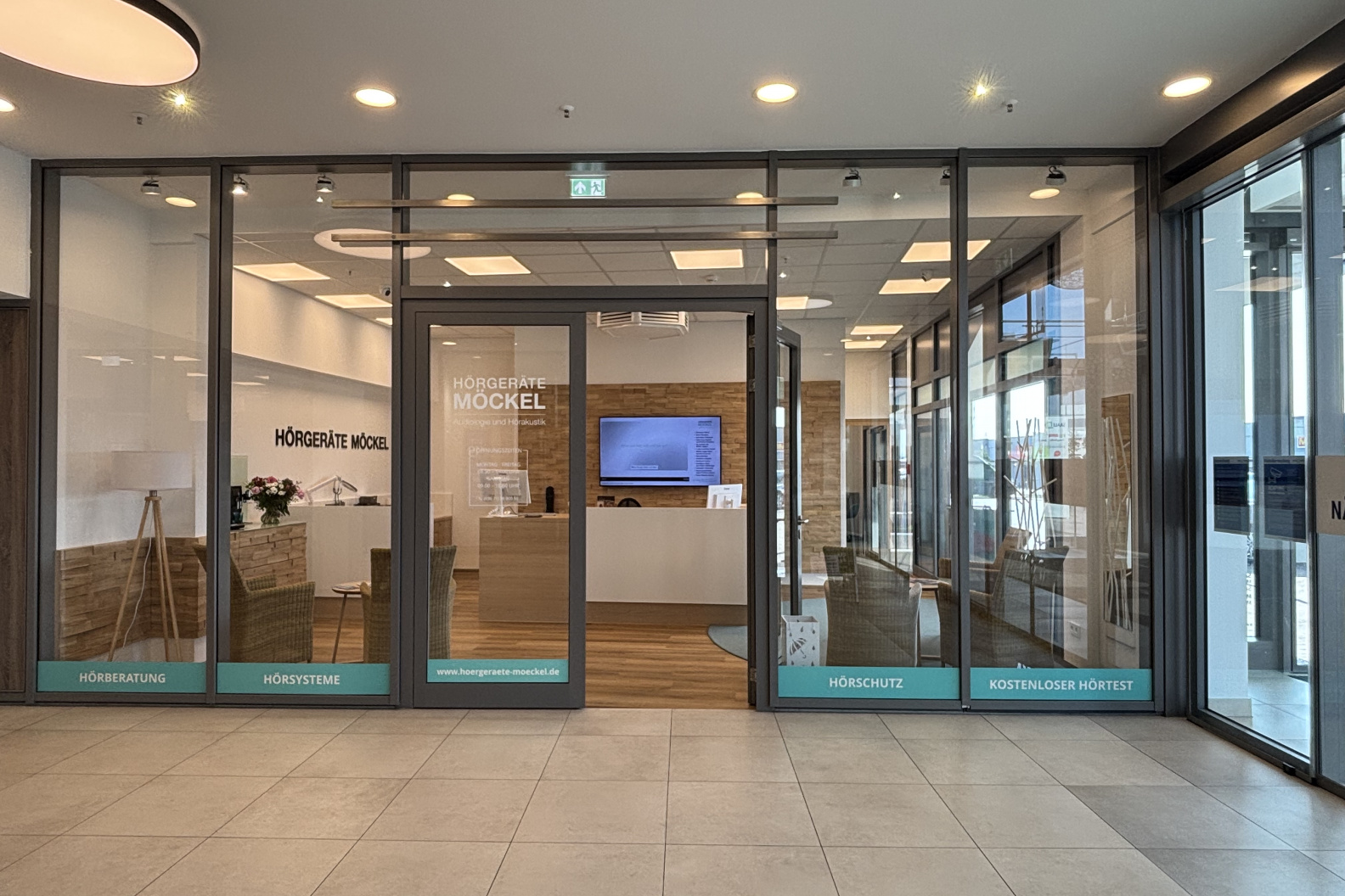 Außenansicht des Fachgeschäfts Hörgeräte Möckel in Saalfeld mit großer Glasfront, Blick auf den Empfangsbereich und Sitzmöglichkeiten im Inneren.