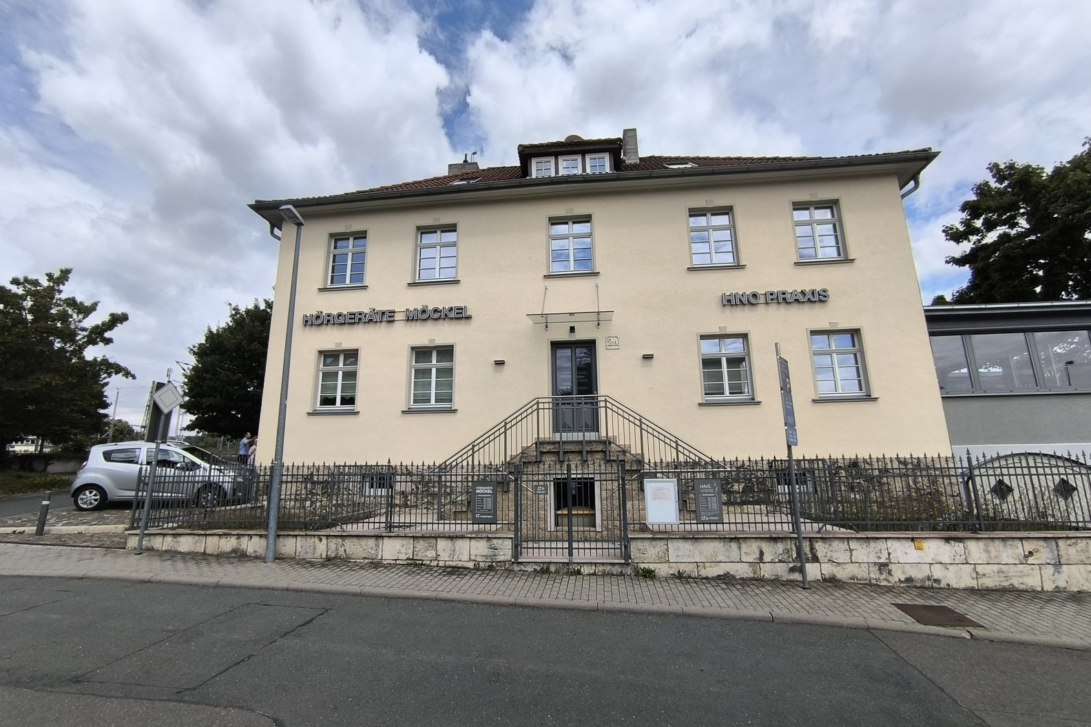 Außenansicht des Gebäudes von Hörgeräte Möckel in Weimar, einem hellen zweistöckigen Haus mit Treppenaufgang und Beschilderung für Hörgeräte Möckel und HNO Praxis.