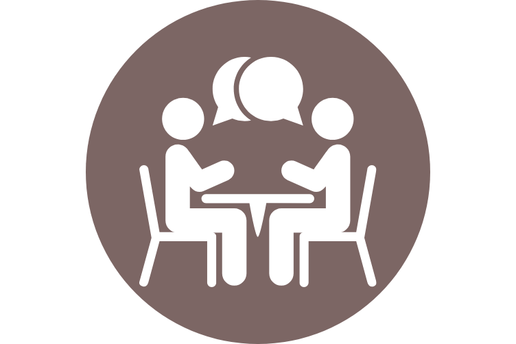 Symbolgrafik mit zwei Personen, die an einem Tisch sitzen und sich unterhalten. Über ihnen sind zwei Sprechblasen dargestellt, die Kommunikation oder Schulung darstellen.