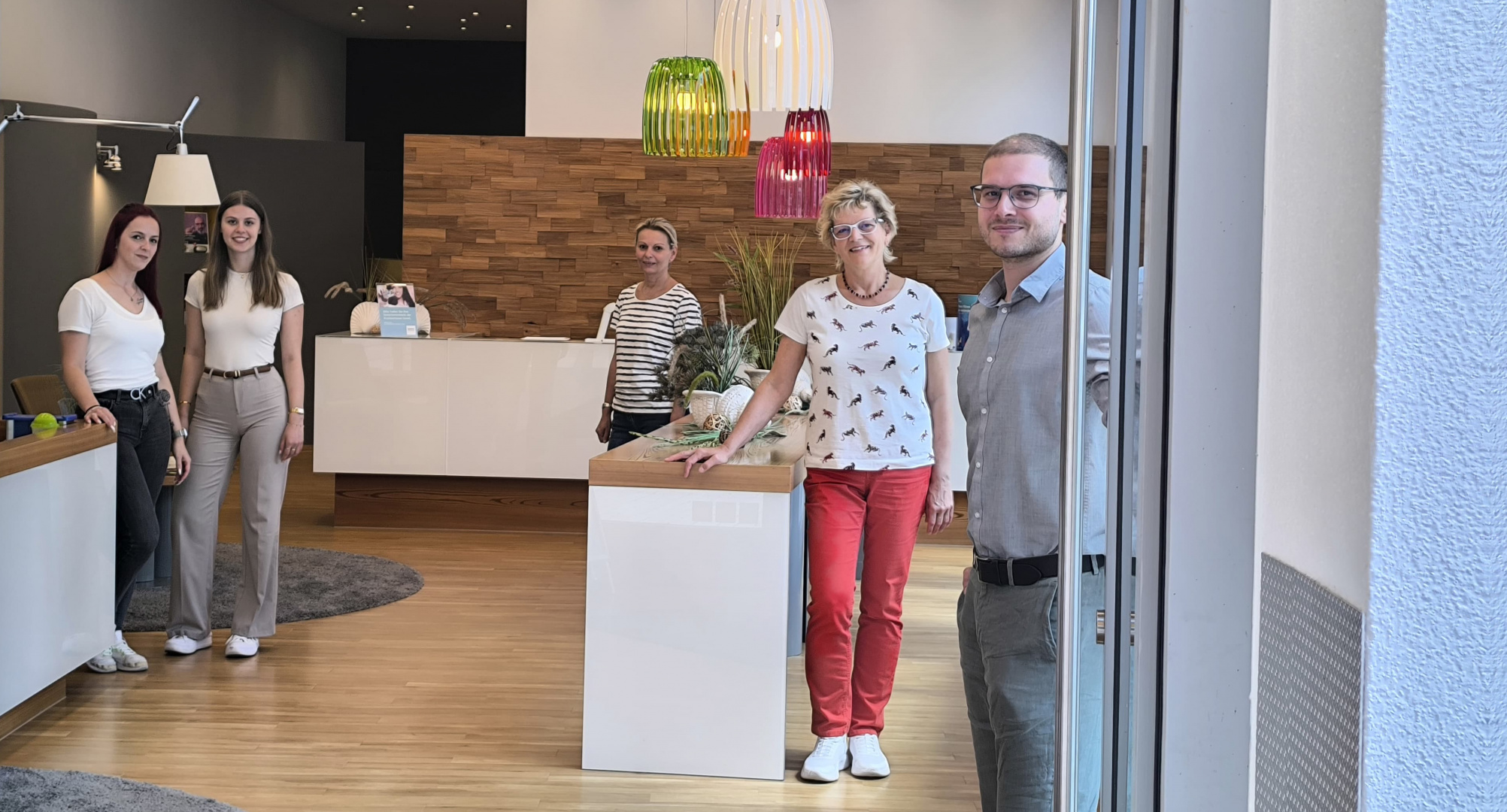 Fünf Teammitglieder von Hörgeräte Möckel Meiningen stehen lächelnd im Eingangsbereich der Filiale in der Georgstraße. Die moderne Einrichtung zeigt Holzdekor, bunte Hängelampen und eine helle Empfangstheke.