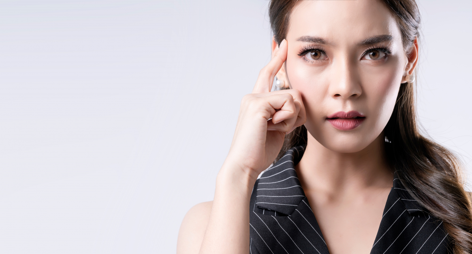 Frau mit ernstem Blick hält nachdenklich zwei Finger an die Schläfe, Nahaufnahme vor hellem Hintergrund.