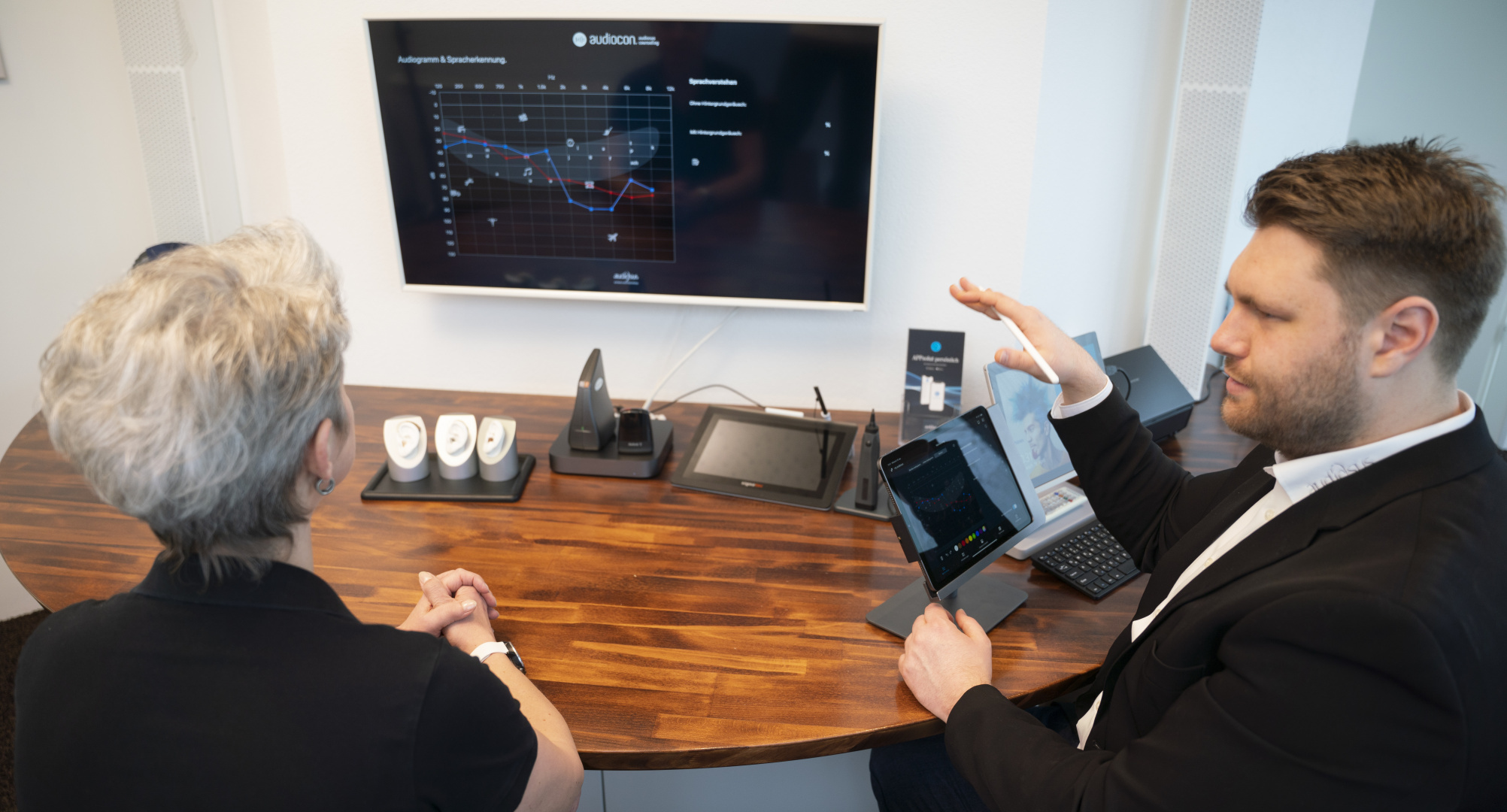 Hörgeräteakustiker erklärt einer Kundin am Bildschirm die Ergebnisse eines Hörtests in der Filiale.
